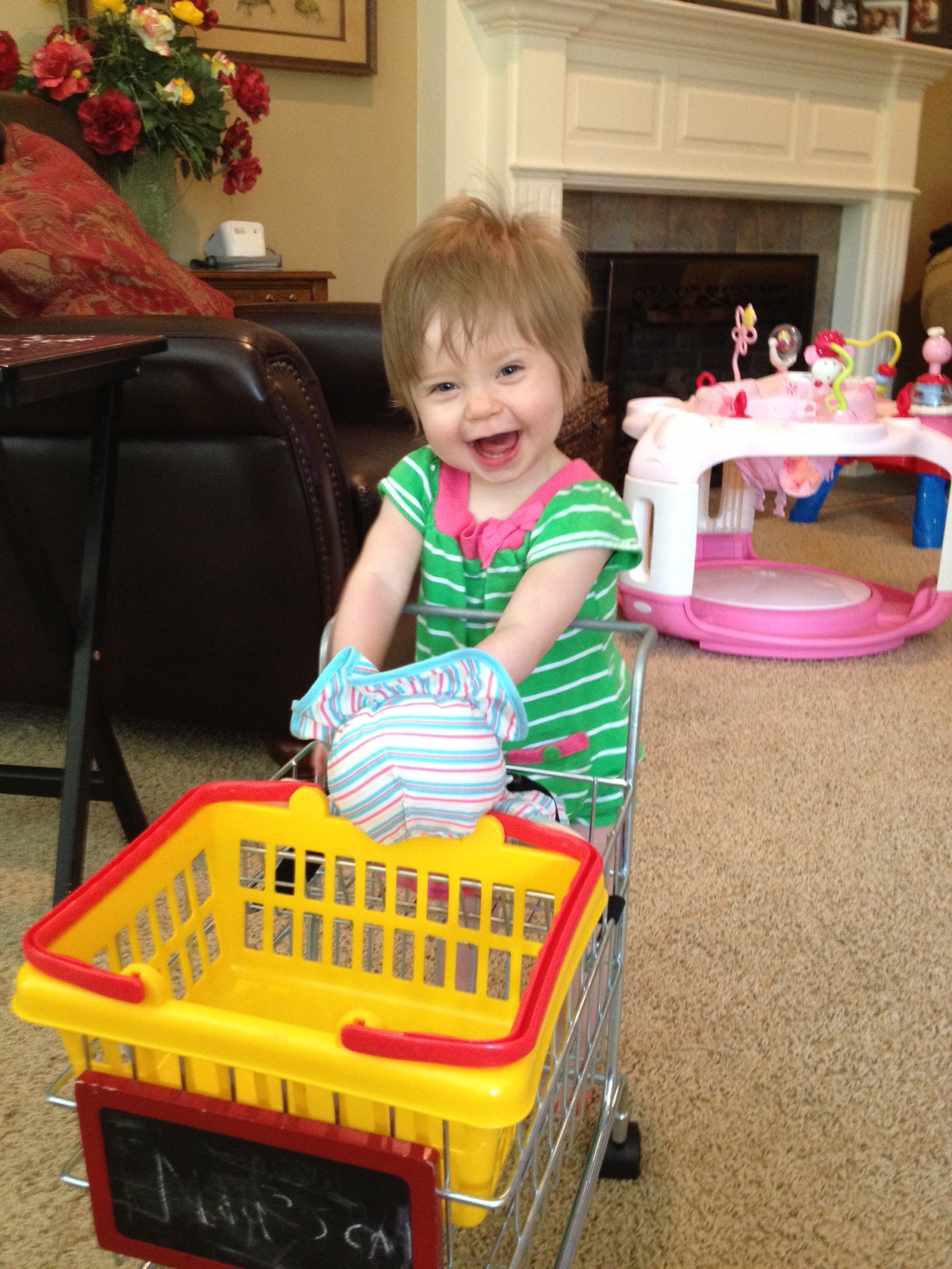 A smiling young girl pushes a toy plastic cart.